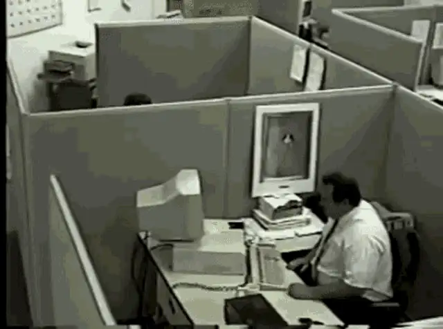 Man in a cubicle beating a keyboard against his monitor